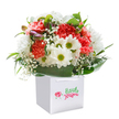 Radiating gentle joy, this artful bouquet appears to capture the very mood of Hampton's blooming gardens in spring. Resting gracefully within a sharp white gift bag, the arrangement is a feast for the senses: lush coral and peach carnations, their frilled petals soft as morning light, nestle against radiant white daisies with vibrant green-gold centers, reminiscent of sunlit meadows near Bushy Park. Wisps of delicate baby's breath, airy and tender, weave between the larger blooms, casting a light mist of innocence and charm over the composition. Along one side, unopened buds edged in purple quietly suggest upcoming surprises, mirroring the sense of anticipation at the heart of each special gift. Deep, glossy green leaves fan outward to cradle the flowers, their bold presence creating a soothing, natural canopy akin to the foliage that lines Hampton's riverside paths. The sturdy white gift bag, topped with elegant ribbon handles, stands at the ready-perfect for local delivery to a friend, loved one, or neighbour. Illuminated by even, natural daylight against a blank canvas, every petal and leaf glows with the freshness and abundant beauty that marks truly local, seasonal floristry. Whether intended for a birthday, a gesture of encouragement, or a congratulatory note, this bouquet from a Hampton florist expresses care, expertise, and heartfelt delight with every stem.